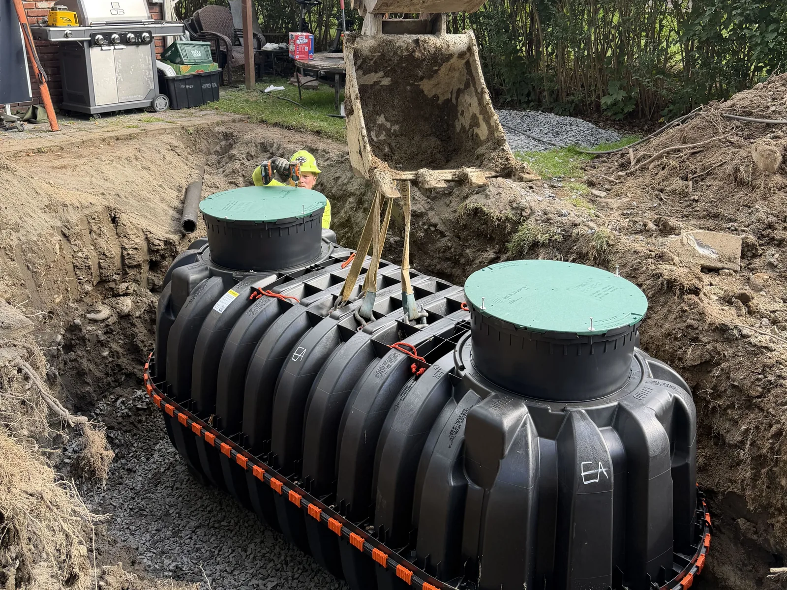 Aerobic septic tank set in the excavation beside a house with the excavator bucket above it