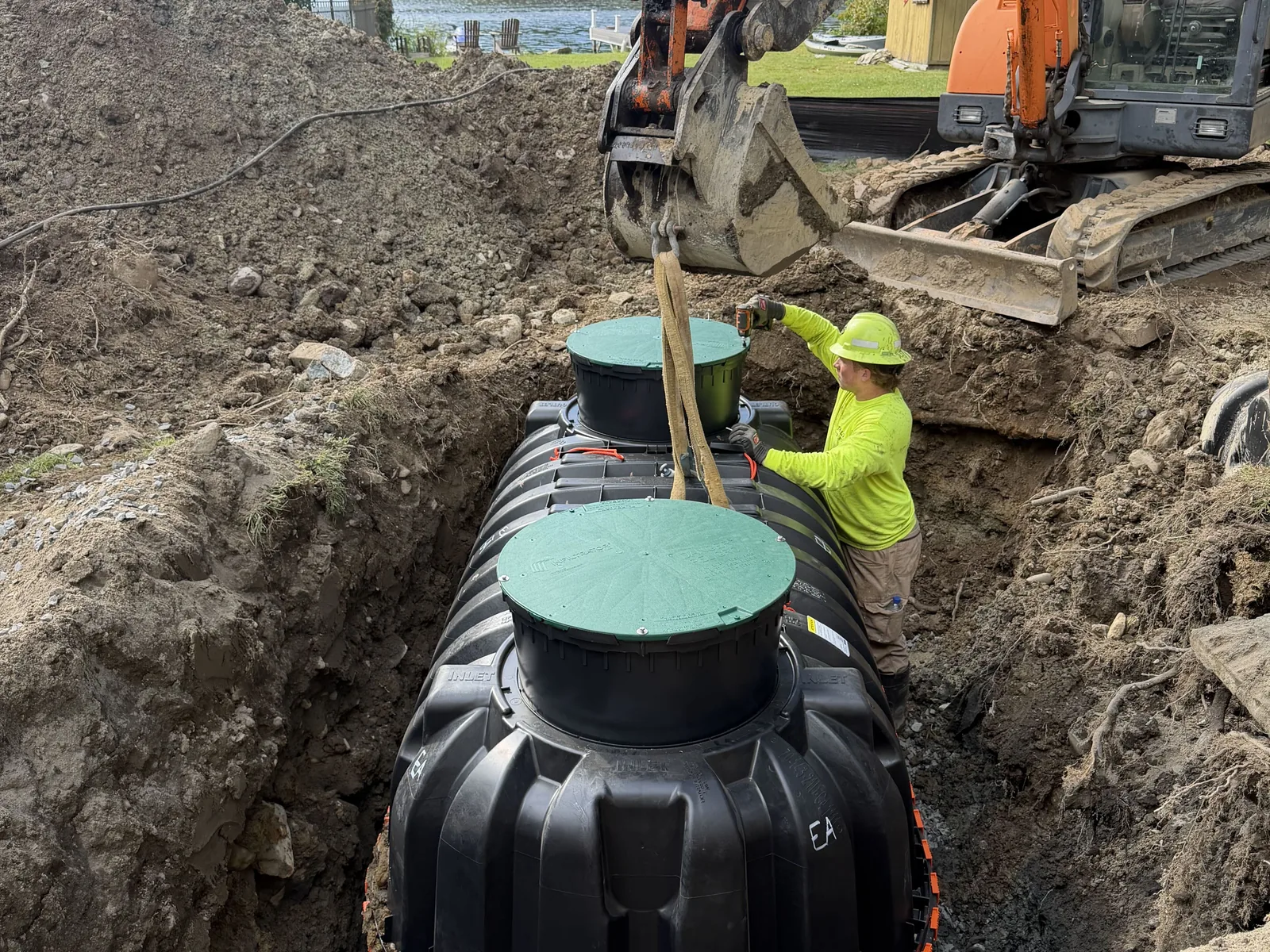 Aerobic treatment unit tank lowered into the hole by our excavator with the lake behind