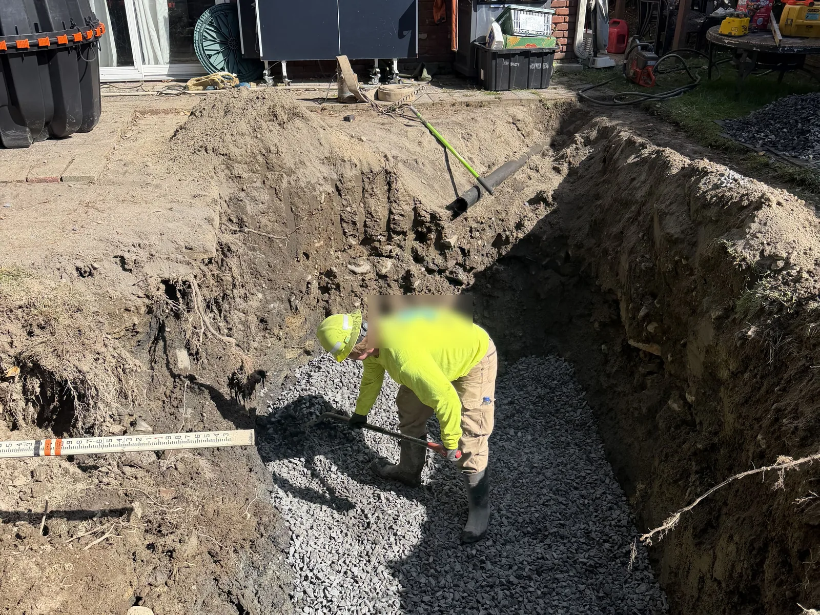 Crushed stone bed being raked level in the tank excavation beside the house