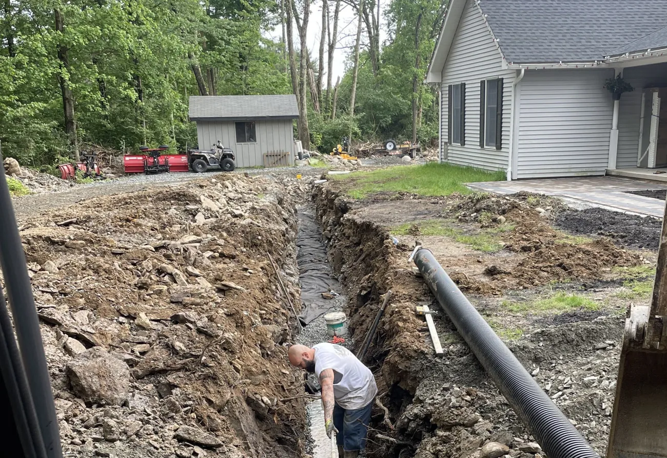 Corrugated drain pipe being laid in a rocky trench beside a house