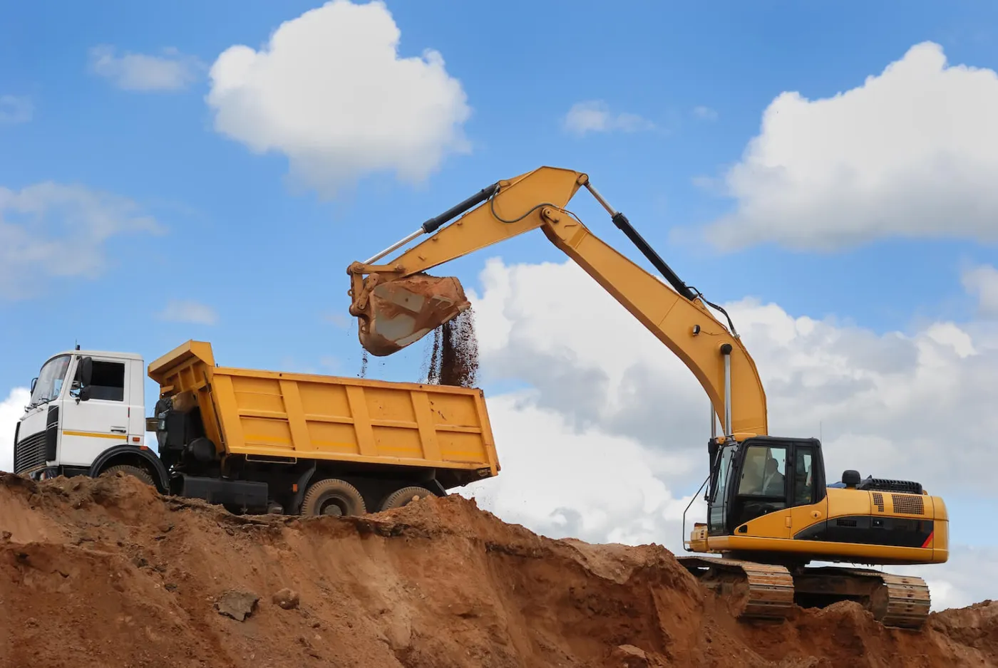 Tracked excavator tipping a bucket of loose soil into a dump truck under open sky
