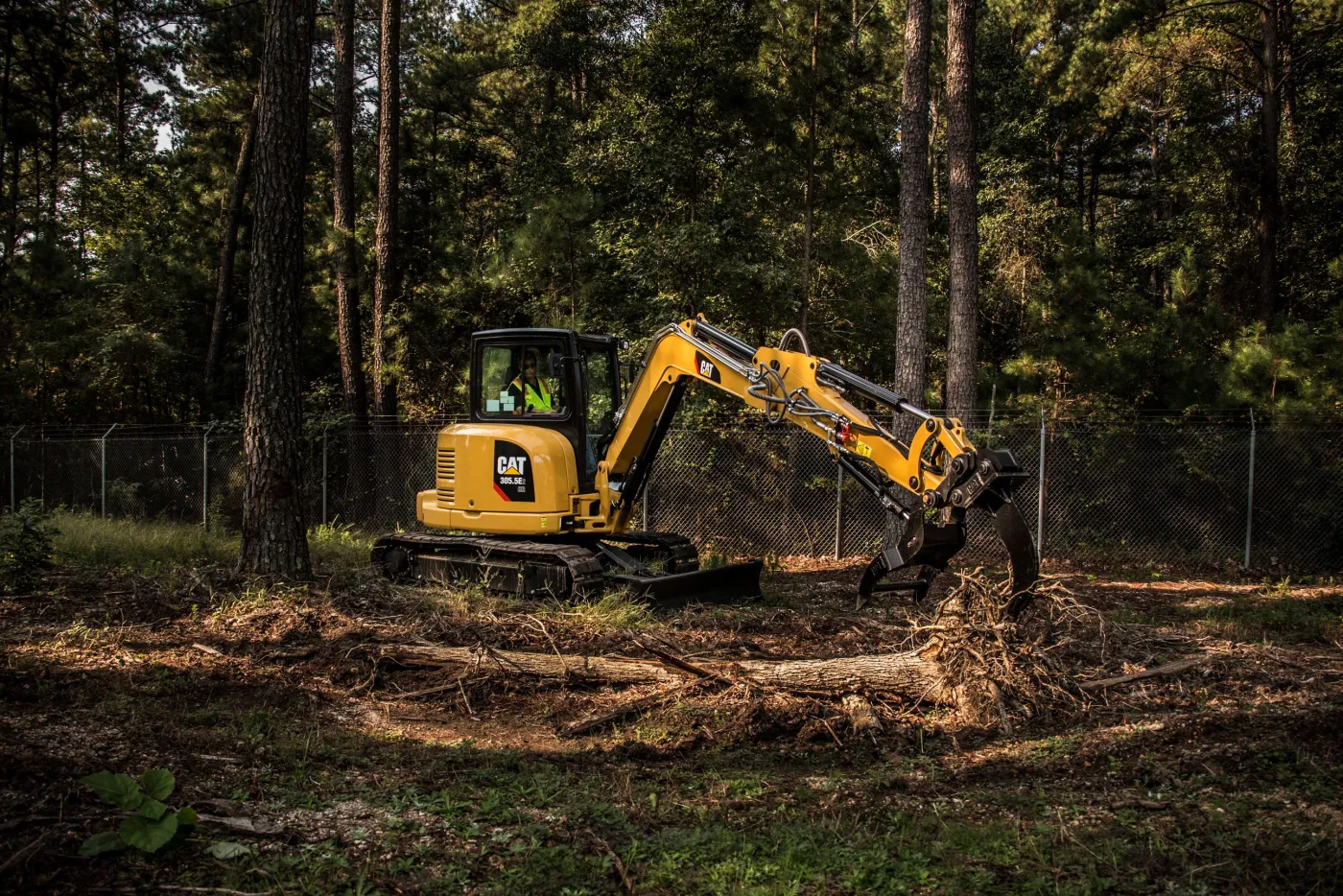 Compact tracked excavator with a grapple attachment moving cut logs and brush inside pine woods