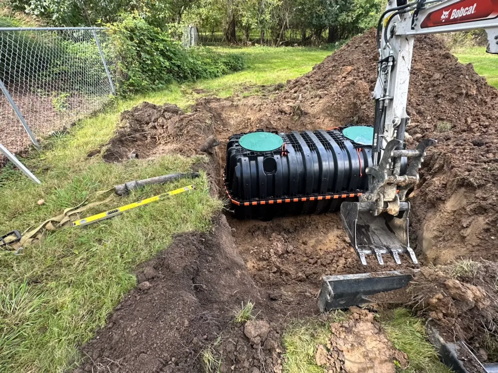 Mini excavator setting a new plastic septic tank into a backyard excavation