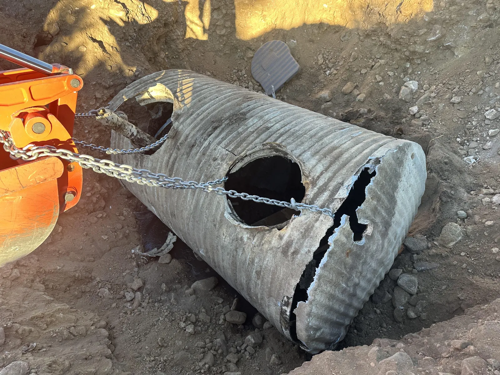 Cracked and rusted corrugated metal septic tank chained up for removal from the ground