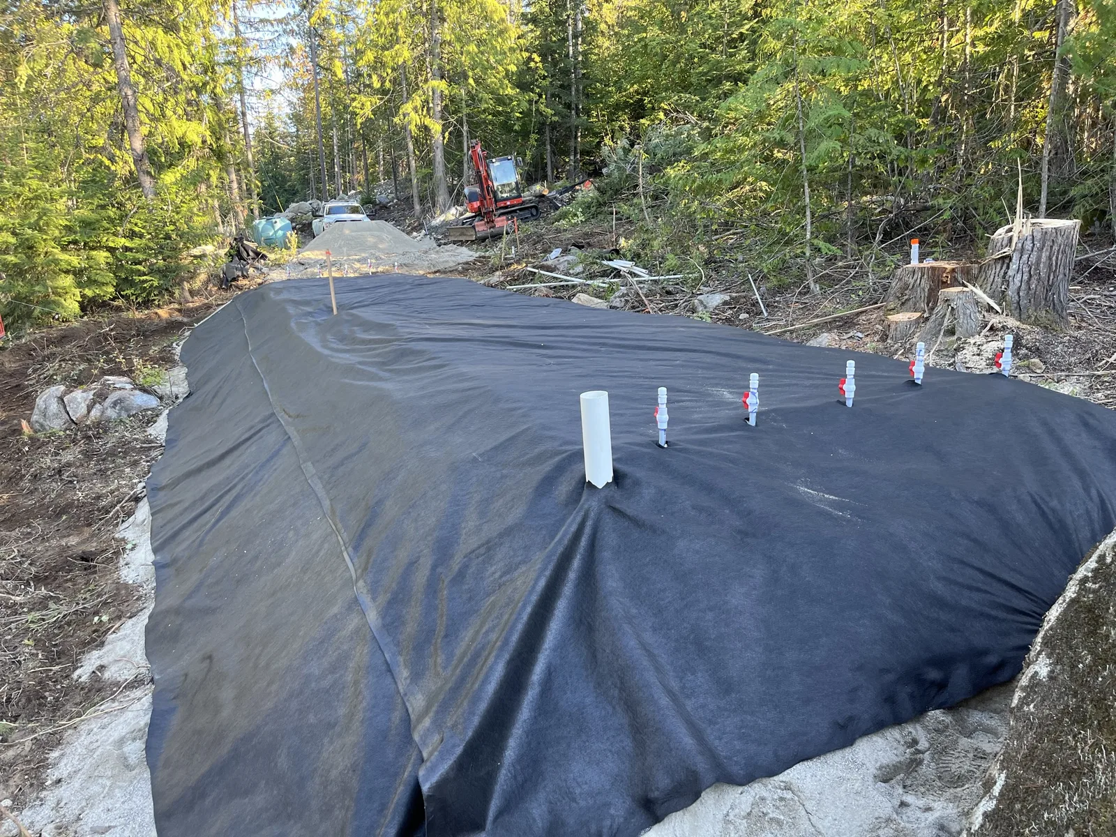 Black filter fabric laid over a finished septic mound with white observation pipes and turn-ups