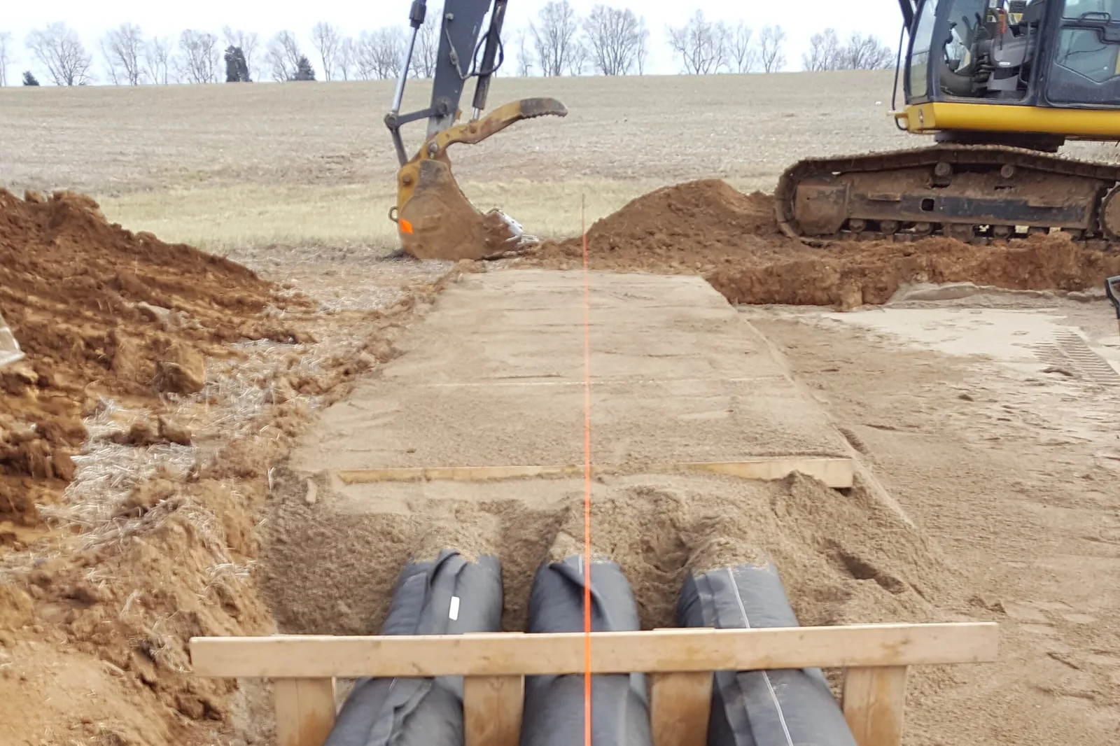 Tracked excavator shaping a sand fill bed with black leaching chambers set in an open field