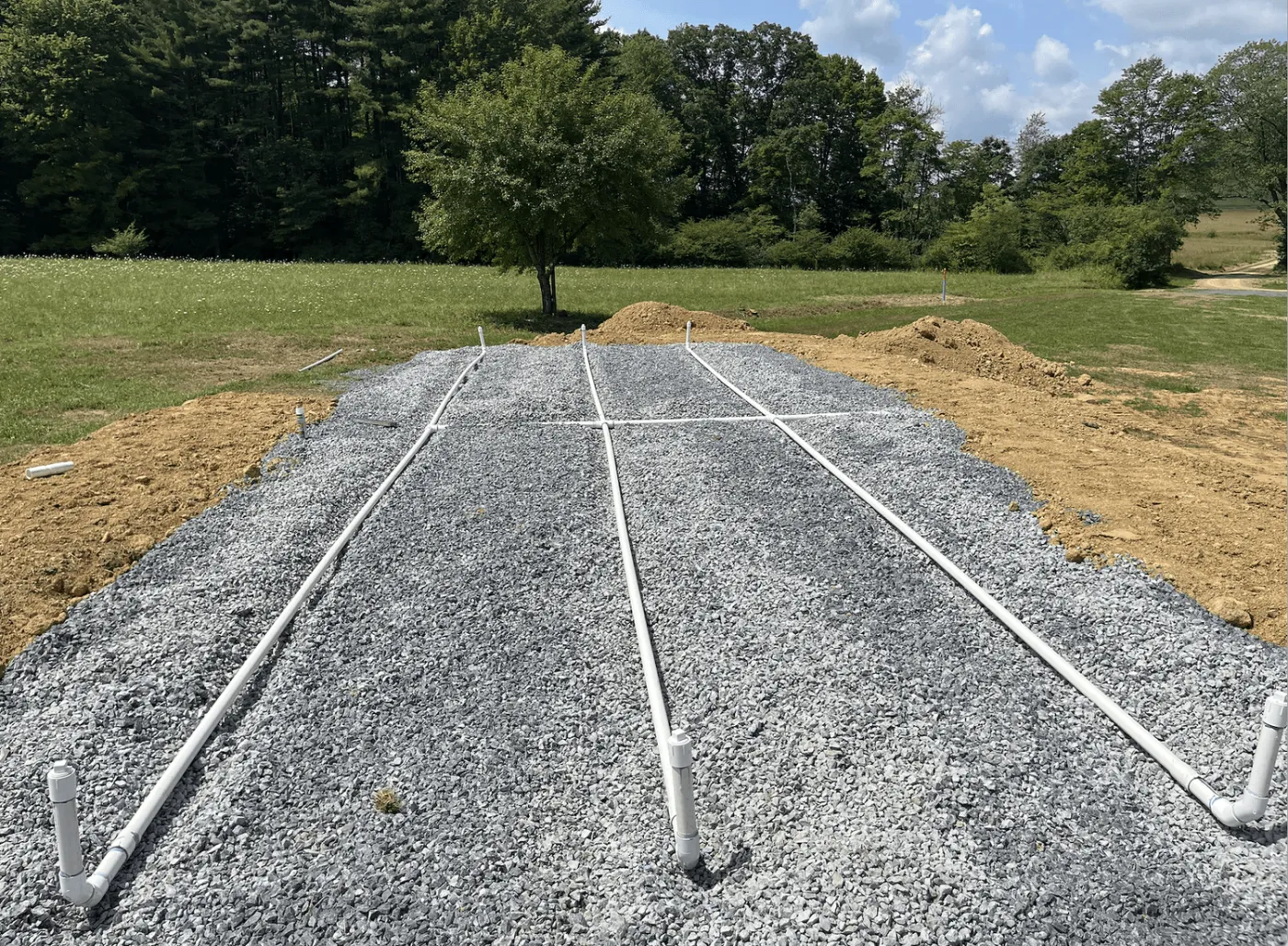 Raised crushed stone septic bed with white perforated laterals and turn ups beside a mowed field