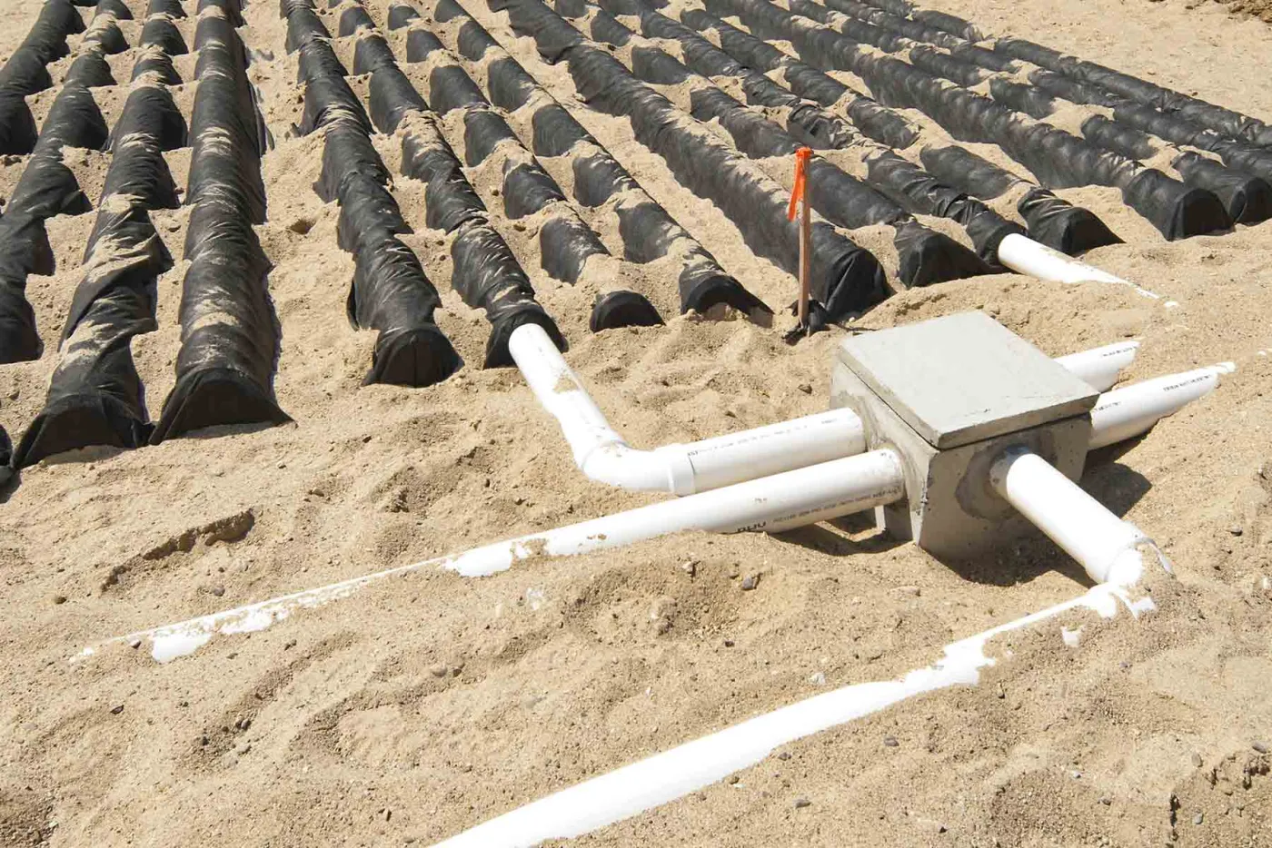 Concrete distribution box with white PVC outlet pipes feeding rows of covered drainfield chambers