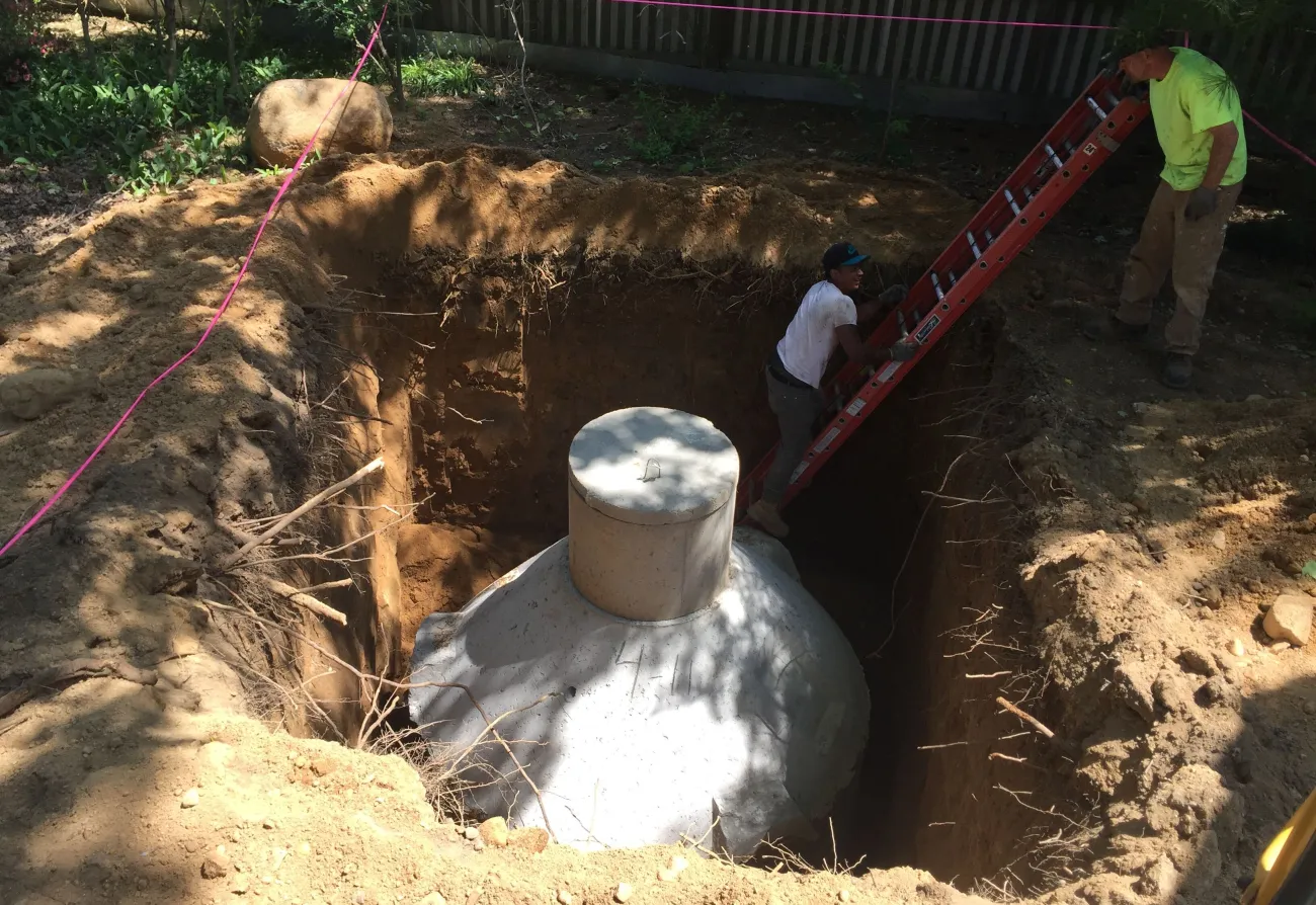 Concrete septic tank set in an open excavation with a worker on a ladder