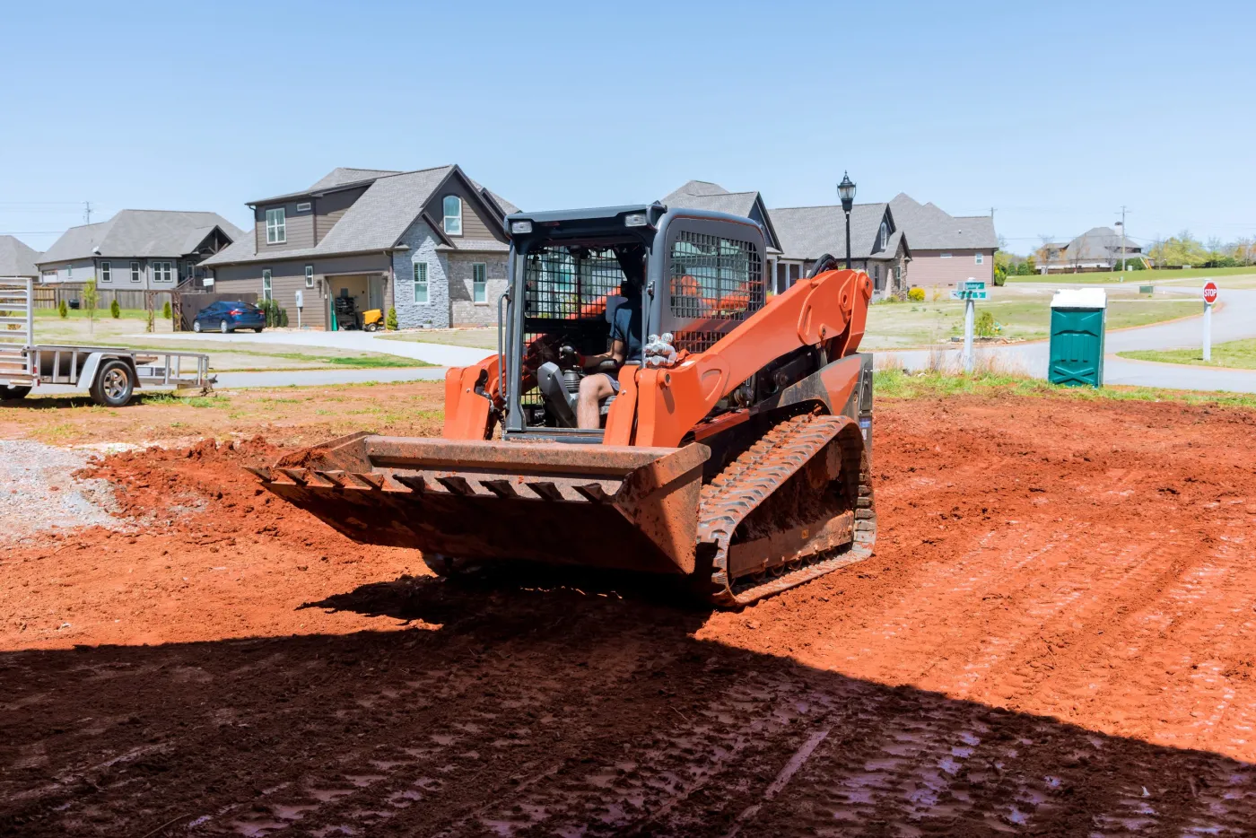 Tracked loader with a bucket smoothing a graded dirt pad on a new residential lot