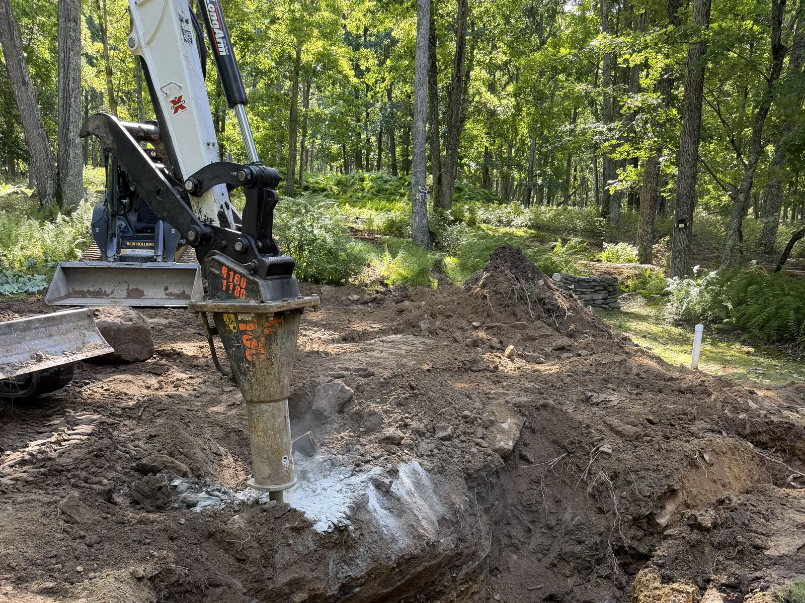 Hydraulic breaker on our skid steer breaking ledge in an open trench